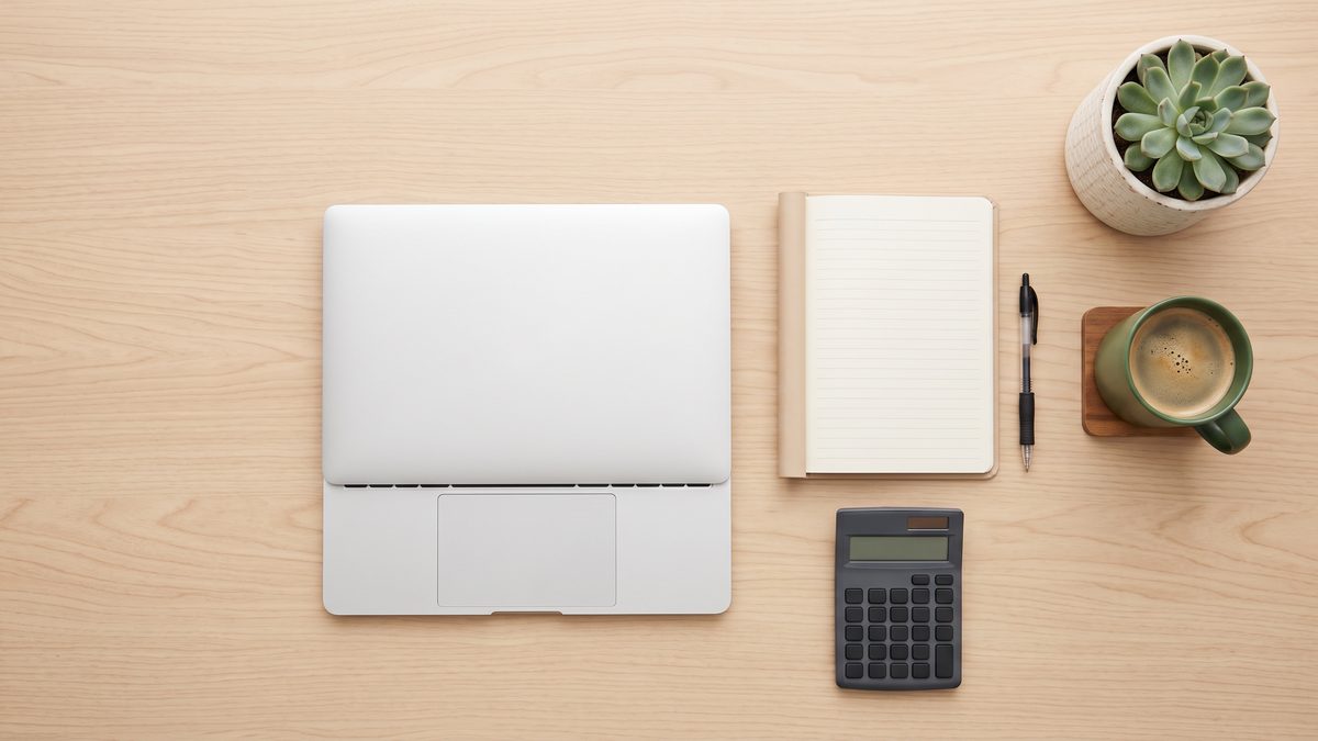 An overhead view of a desk with a laptop, calculator and notebook
